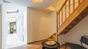 A modern interior with a wooden staircase, a round table with a mat, and a black chair.