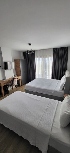 A hotel room with two beds, a desk with a chair, a TV, and a wardrobe. - Kaizen Otel (Erdemli)