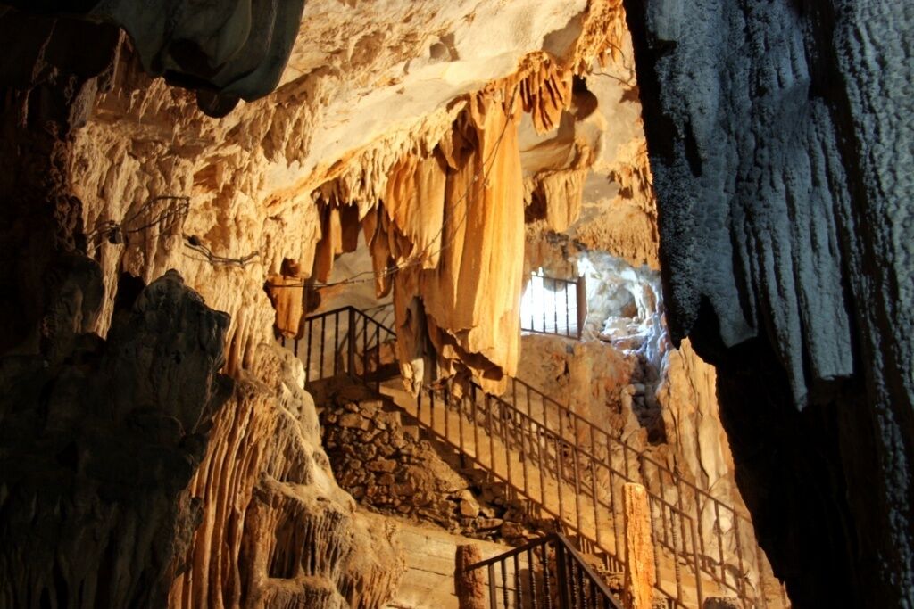 A cave interior with natural rock formations, a staircase, and a metal railing.