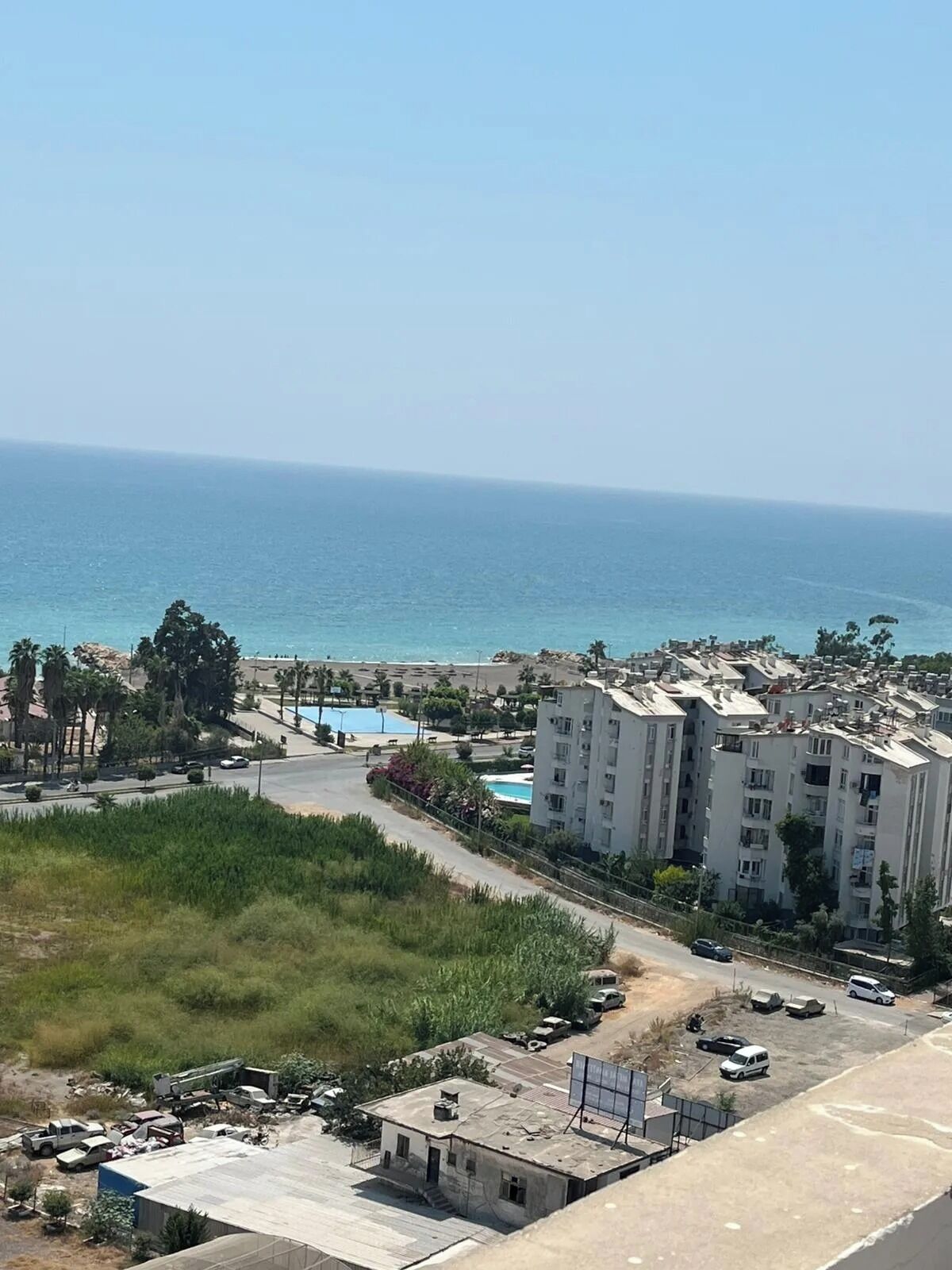 A coastal residential area with a large building complex, a swimming pool, and a road leading to the beach.