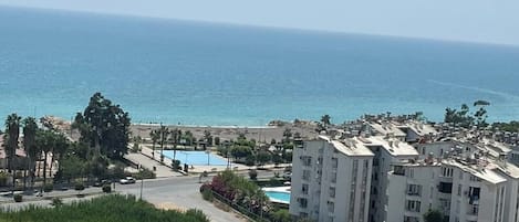 A coastal residential area with a large building complex, a swimming pool, and a road leading to the beach.