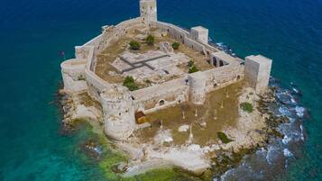 Vista aérea de una fortificación histórica con un patio central, rodeada de muros y torres, situada en una isla rocosa con aguas azul turquesa.