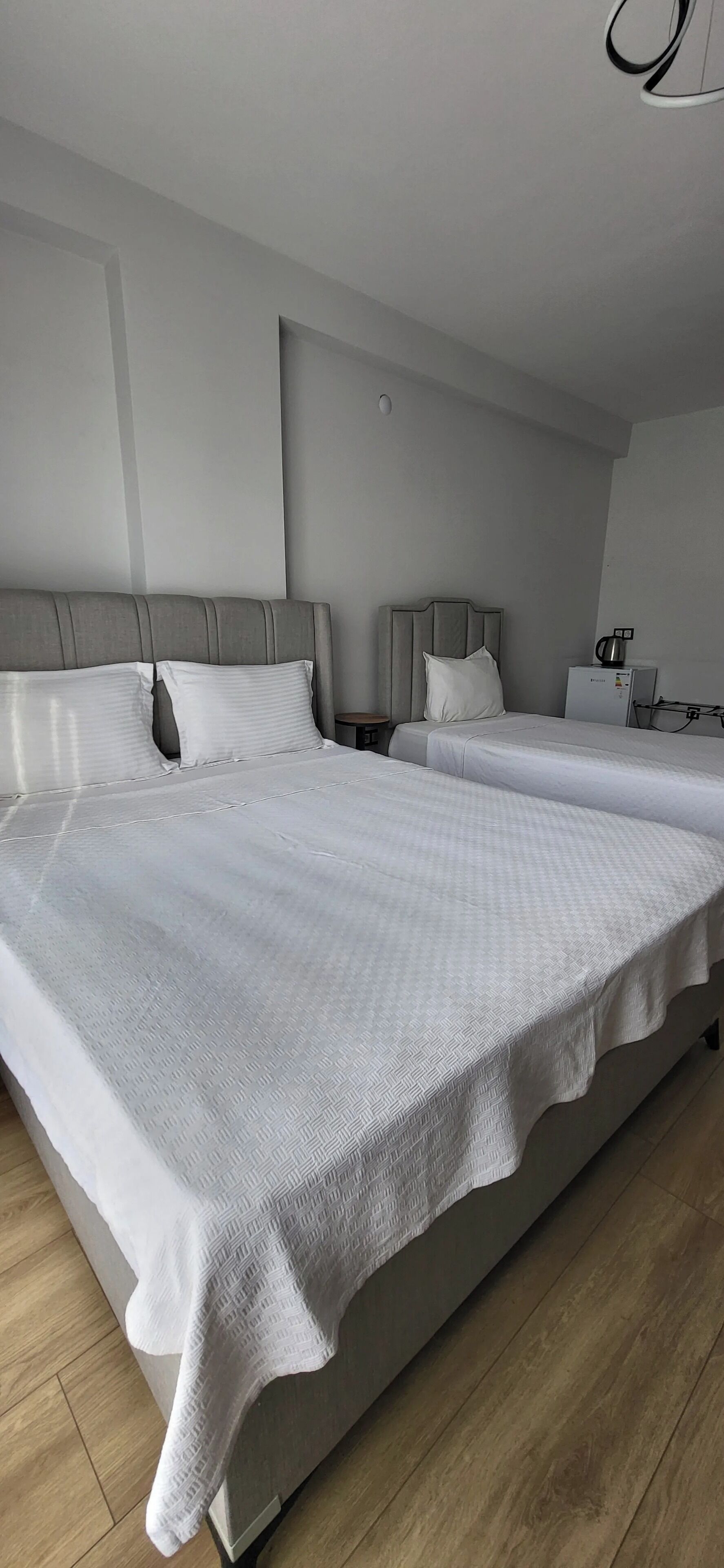 A modern hotel room with two large beds, a small table, and a refrigerator.