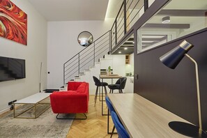 A modern living room with a red sofa, a wooden dining table, and a staircase leading to an upper level. - Duplex Center of Paris (Paris)