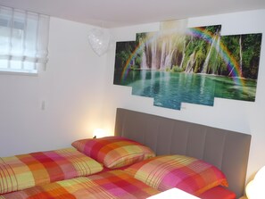A bedroom with a bed, two pillows, a window, and a wall with a rainbow and waterfall painting. - Apartment 'Carpe Diem' with Shared Terrace, Shared Garden and Wi-Fi (Rust)