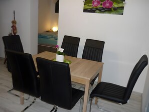 A dining area with a wooden table, black chairs, and a small potted plant with a pink flower. - Apartment 'Carpe Diem' with Shared Terrace, Shared Garden and Wi-Fi (Rust)