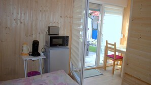 A compact room with a bed, a small table with a microwave and coffee maker, a chair, and a sliding door leading to an outdoor area. - Tiny Home 'Am See' with Shared Terrace, Garden and Wi-Fi (Rust)