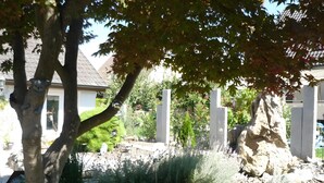 A garden with a stone wall, a tree, and a white fence. - Tiny Home 'Am See' with Shared Terrace, Garden and Wi-Fi (Rust)