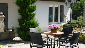 An outdoor patio with a round table and four chairs, surrounded by potted plants and a large tree. - Tiny Home 'Am See' with Shared Terrace, Garden and Wi-Fi (Rust)