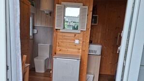 A compact kitchen with wooden walls, a refrigerator, a sink, and a window with a view of greenery. - Tiny Home 'Am See' with Shared Terrace, Garden and Wi-Fi (Rust)