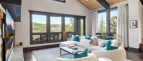A spacious living room with a large sectional sofa, a coffee table, and a view of a mountainous landscape through large windows.