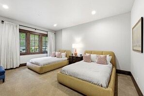 A hotel room with two beds, a nightstand, a lamp, and a window with curtains.