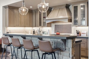 Een moderne keuken met een centraal eiland, barkrukken en hanglampen.