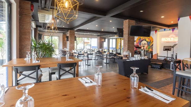 A spacious restaurant with wooden tables, hanging geometric light fixtures, and a large mural on the wall. - The Strype Hotel (Tagaytay)