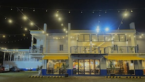 A two-story building with a yellow awning, outdoor seating area, and string lights. - The Strype Hotel (Tagaytay)