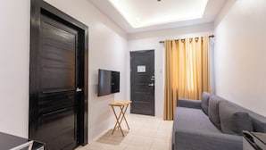 A modern living room with a grey sofa, a small wooden table, a flat-screen TV mounted on the wall, and two black doors. - The Strype Hotel (Tagaytay)