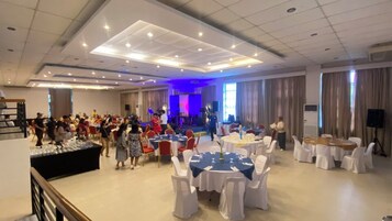 A banquet hall with round tables covered in white tablecloths, a stage with musical instruments, and a crowd of people.