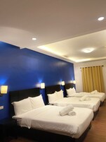 A hotel room with three beds, blue walls, and recessed ceiling lights.