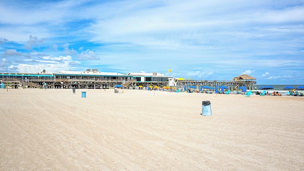 A beach with a pier extending into the water, featuring a restaurant and seating areas.