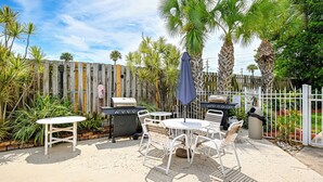 An outdoor patio with a round table and chairs, a grill, and a wooden fence.