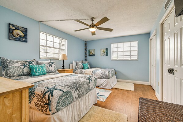 A bedroom with two beds, a ceiling fan, and a large window.