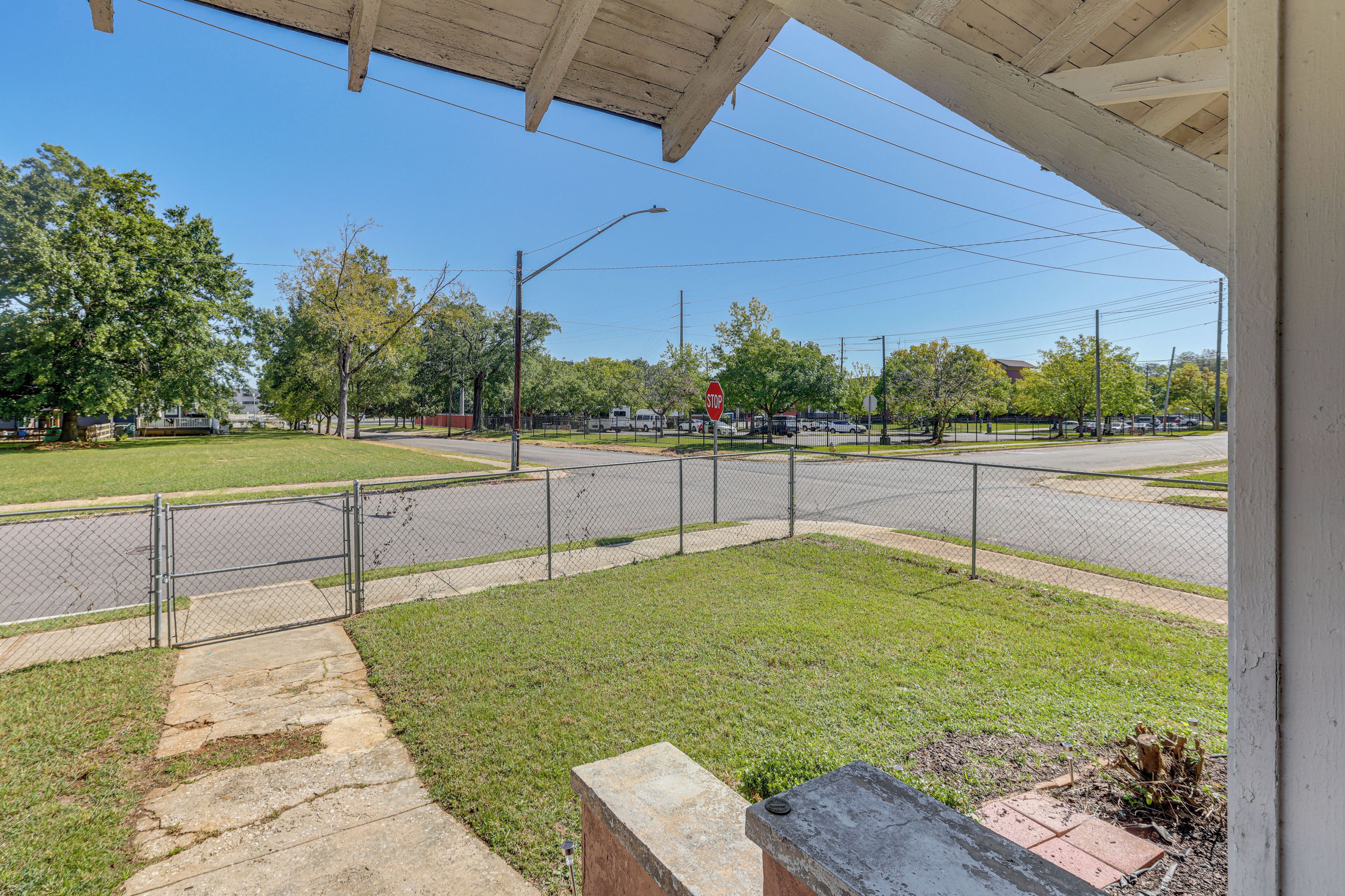 A view from a porch overlooking a street with a stop sign, a chain-link fence, and a grassy area.