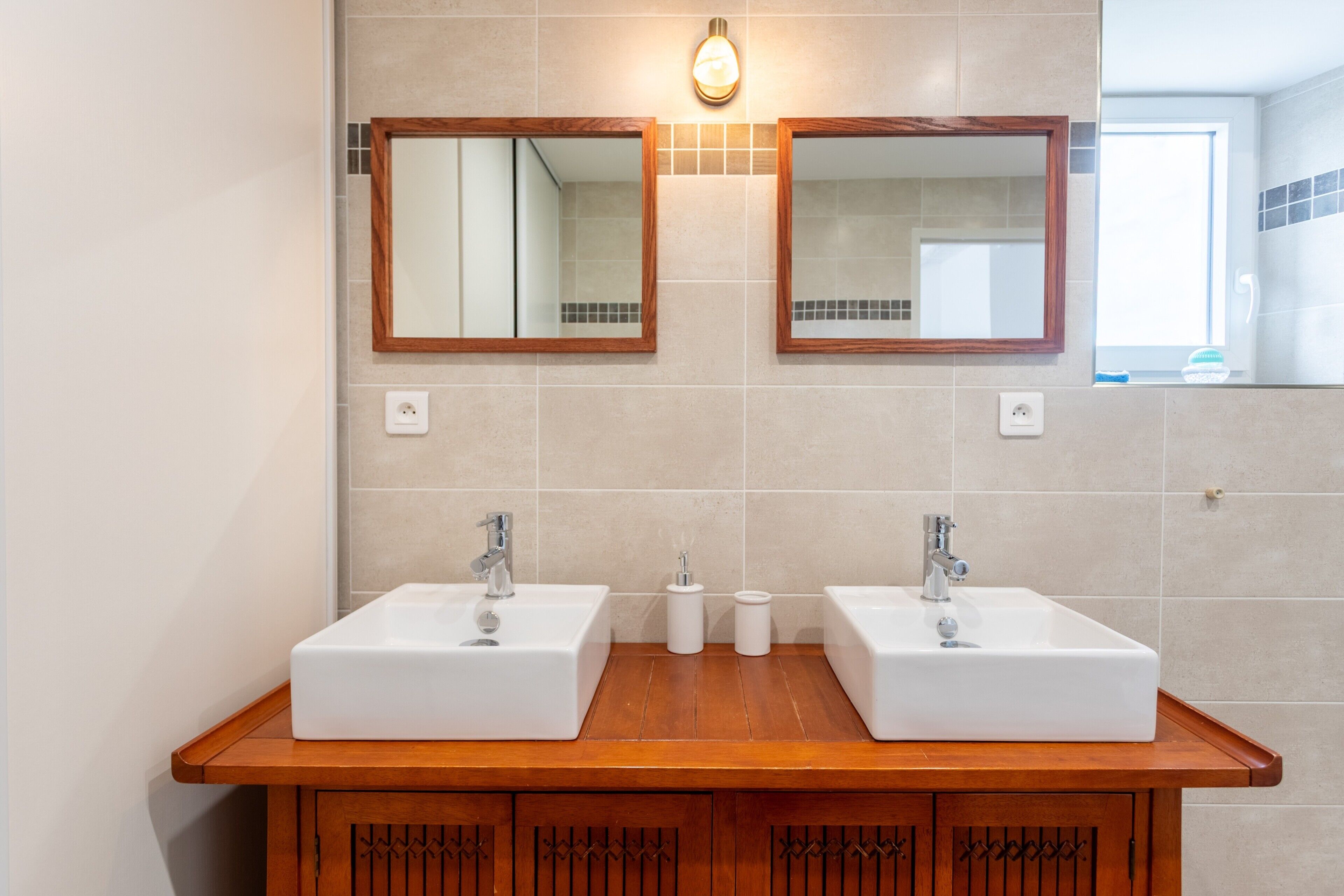 Un baño con dos lavamanos, tocador de madera y dos espejos fijados a la pared.
