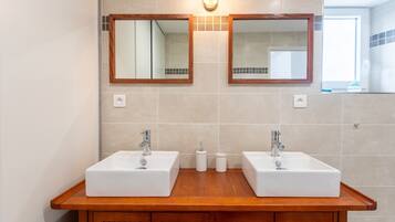 Un baño con dos lavamanos, tocador de madera y dos espejos fijados a la pared.