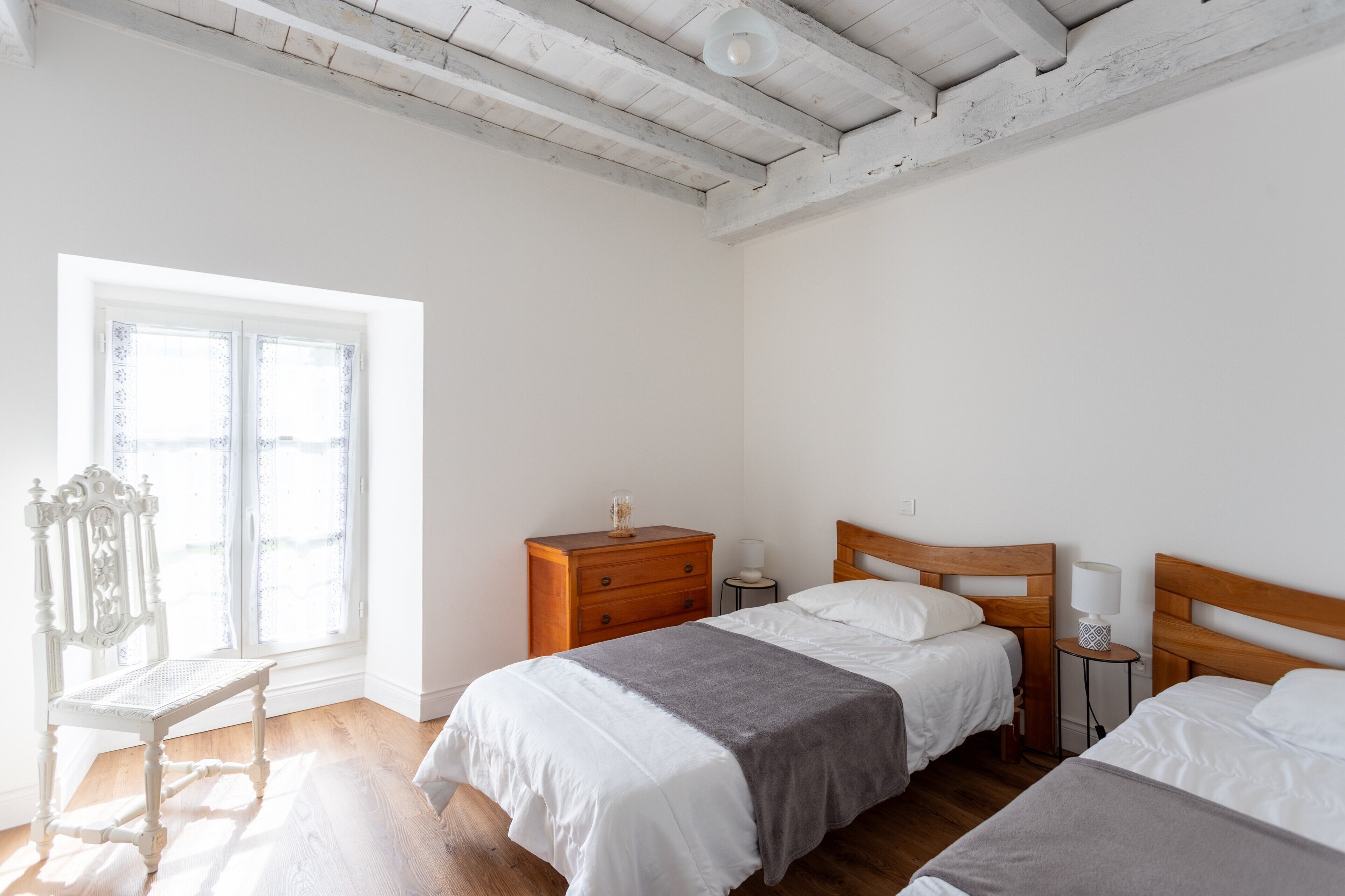 A bedroom with two beds, a wooden nightstand, a chair, and a window with a view.