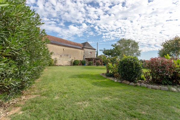 A building with a sloped roof, a grassy yard, and a variety of shrubs and trees.
