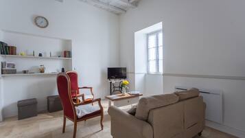 A living room with a sofa, a red chair, a television, a bookshelf, and a window.