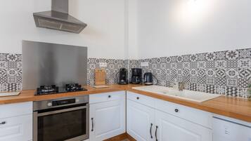Eine moderne Küche mit Edelstahlherd, Backofen und Geschirrspüler, weißen Schränken und einer belegten Spritzschutzwand.