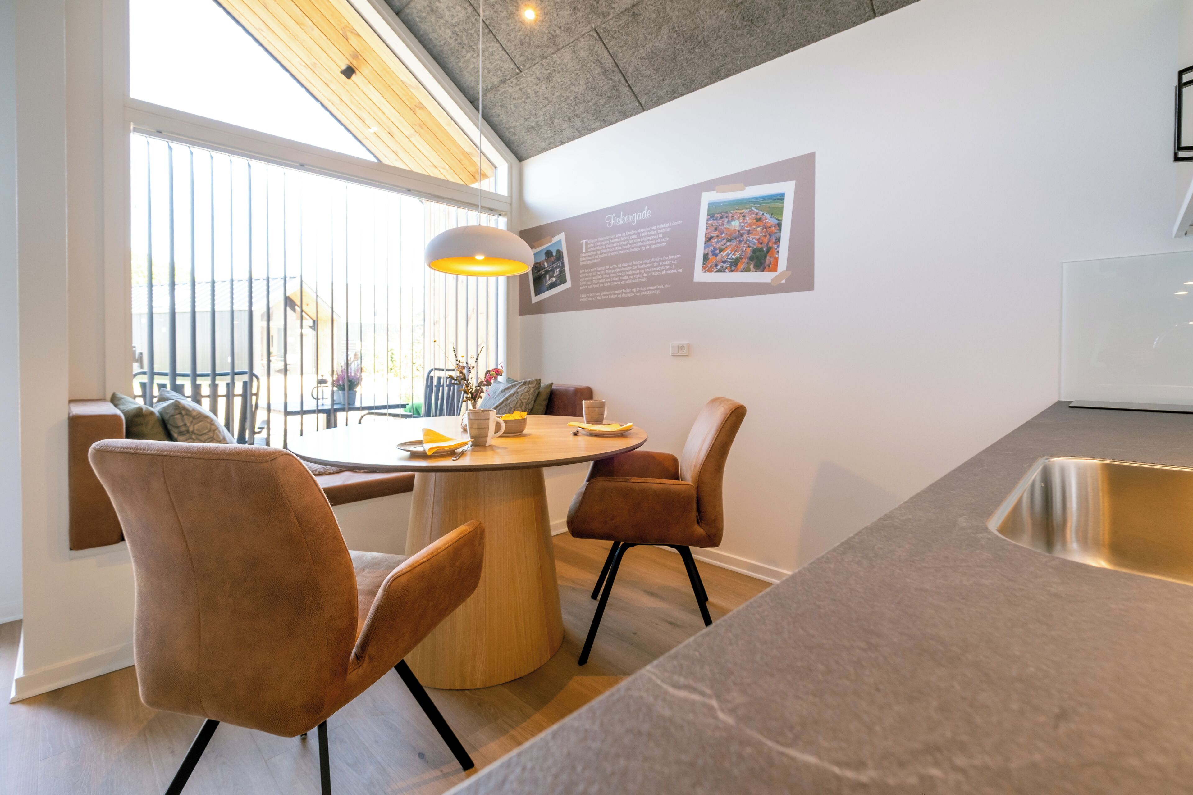 A modern kitchen with a round dining table, two brown chairs, and a large window with blinds.