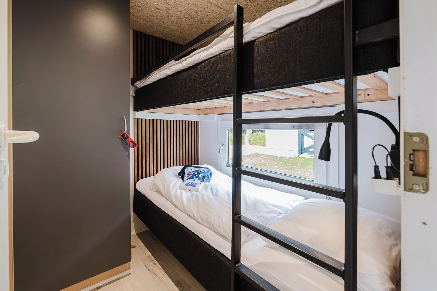 Ein Schlafzimmer mit Etagenbett, Fenster, Nachttisch und einer Sonnenbrille, die an der Wand hängt.