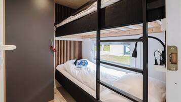 Ein Schlafzimmer mit Etagenbett, Fenster, Nachttisch und einer Sonnenbrille, die an der Wand hängt.