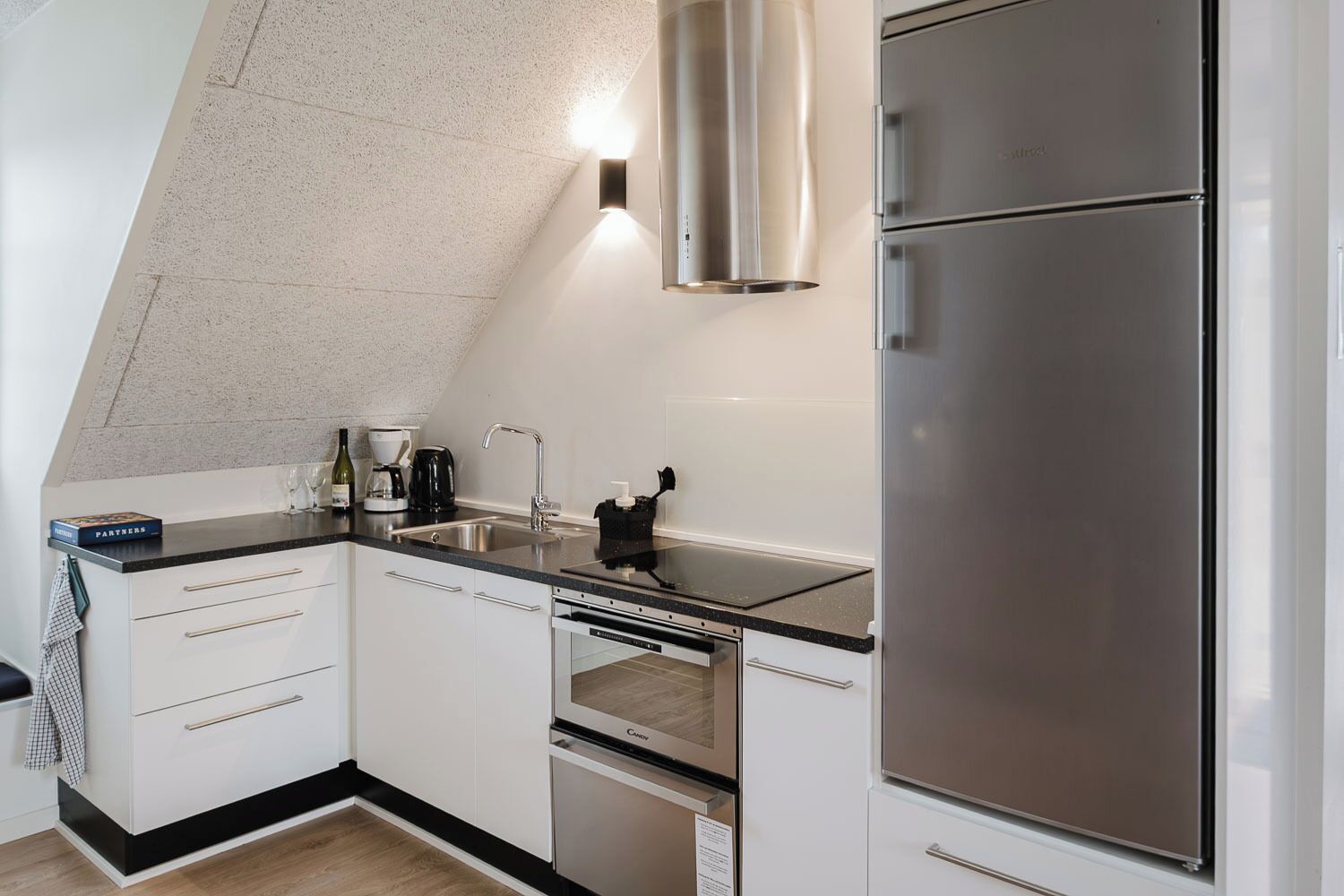 Una cocina moderna con un refrigerador de acero inoxidable, horno empotrado y lavavajillas. Hay una encimera negra y un salpicadero blanco.