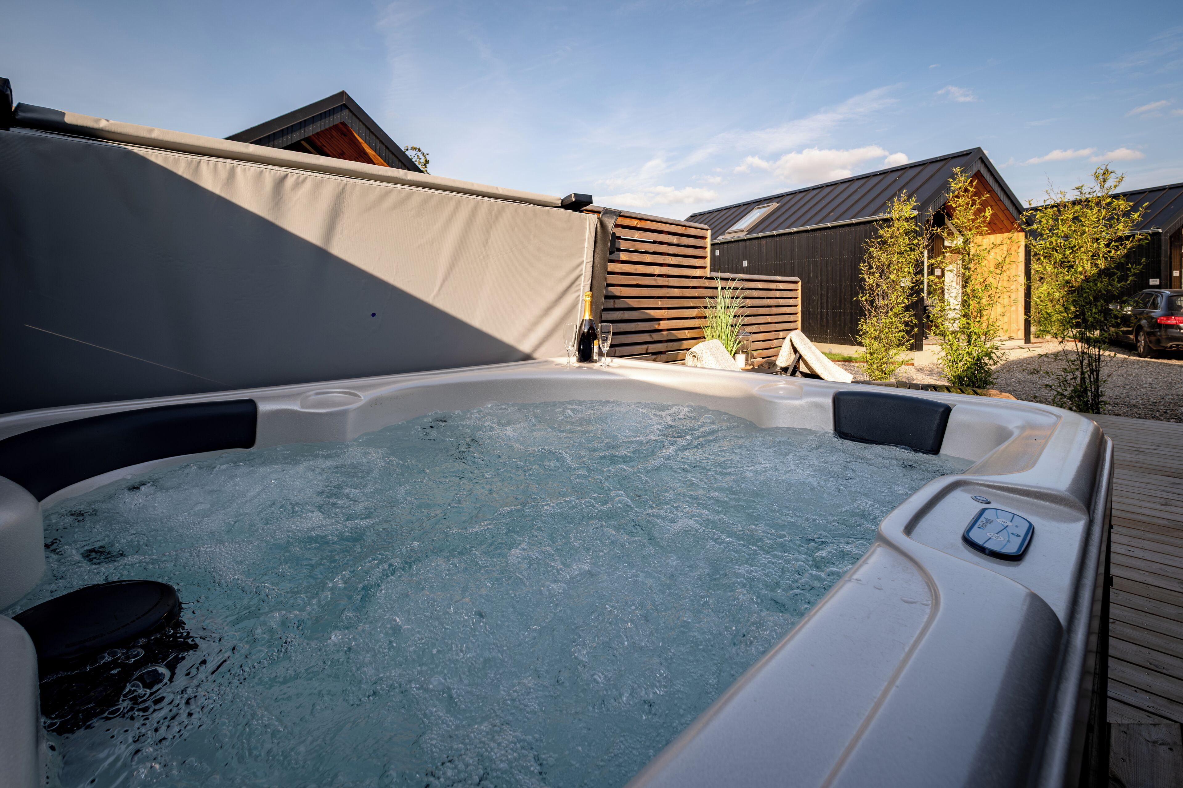 Een hottub met bedieningspaneel, omgeven door een houten terras en een overdekt gebied.