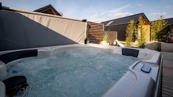 Een hottub met bedieningspaneel, omgeven door een houten terras en een overdekt gebied.