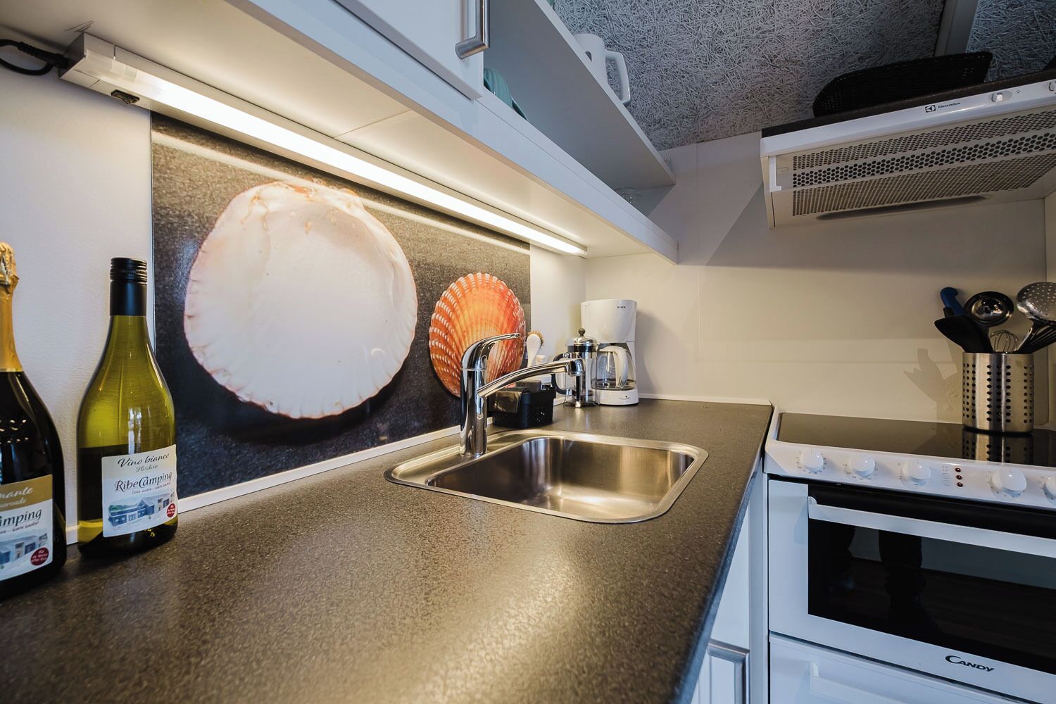 A kitchen with a stainless steel sink, a coffee maker, and a microwave. There are two wine bottles on the counter.