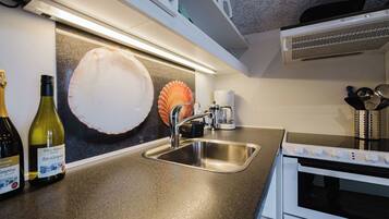 A kitchen with a stainless steel sink, a coffee maker, and a microwave. There are two wine bottles on the counter.
