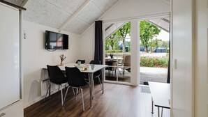 A dining area with a table and chairs, a flat-screen TV mounted on the wall, and a view of the outdoor patio. - Ribe Camping (Ribe)
