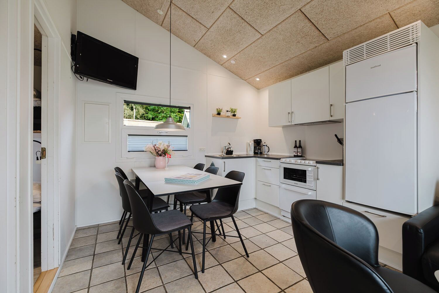 Une cuisine compacte avec des meubles blancs, un four encastré et un réfrigérateur blanc.