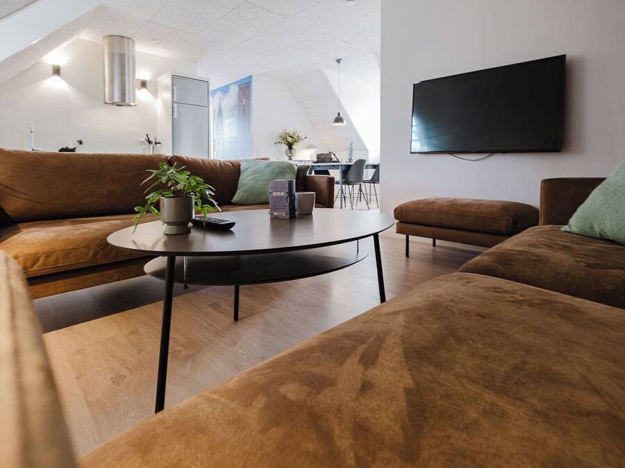 Una sala de estar moderna con sofás marrones, una mesa redonda de centro y un televisor de pantalla plana montado en la pared.