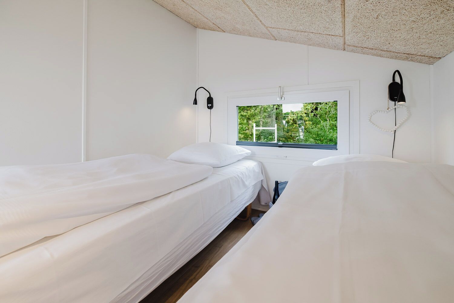Een kamer met twee eenpersoonsbedden, witte muren, een raam met uitzicht op groen en twee wandlampen.