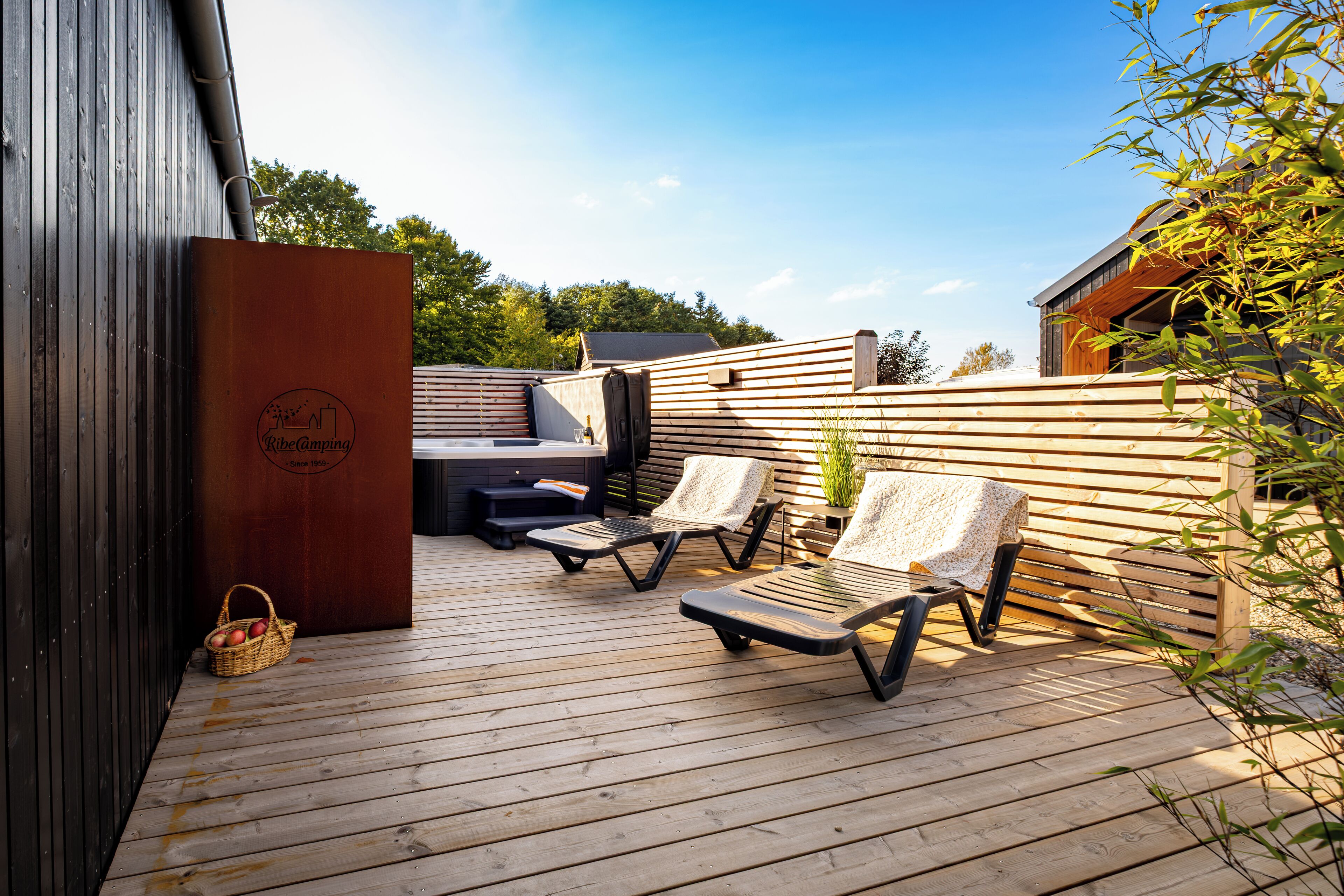 An outdoor deck with wooden flooring, two lounge chairs, a small table, and a basket of apples.