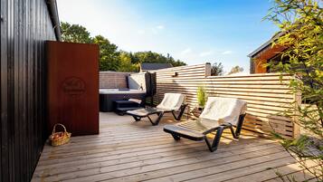 An outdoor deck with wooden flooring, two lounge chairs, a small table, and a basket of apples.