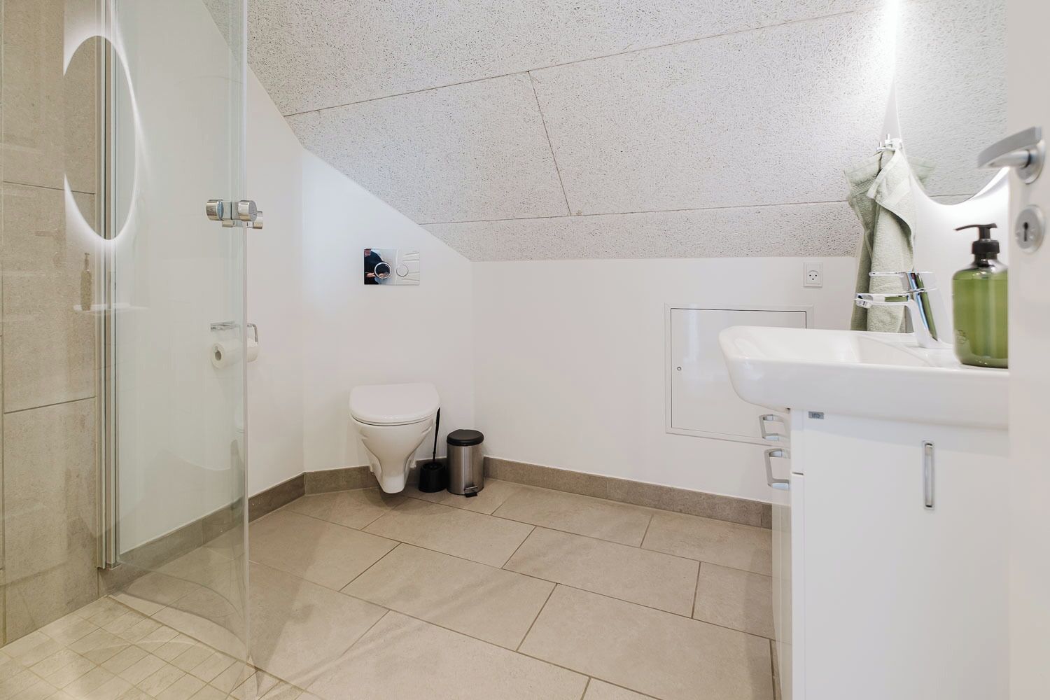 Une salle de bain moderne avec une douche à parois de verre, des toilettes, une poubelle et un lavabo avec un miroir.