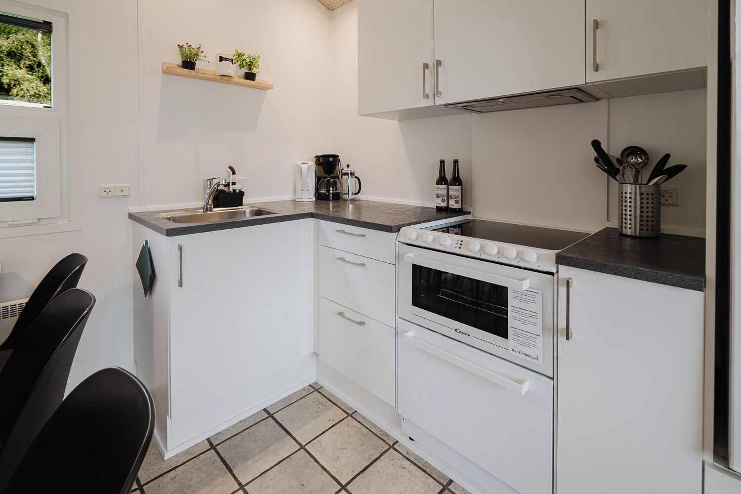 Eine moderne Küche mit weißen Schränken, einem Backofen, einer Kaffeemaschine und einem Spülbecken.