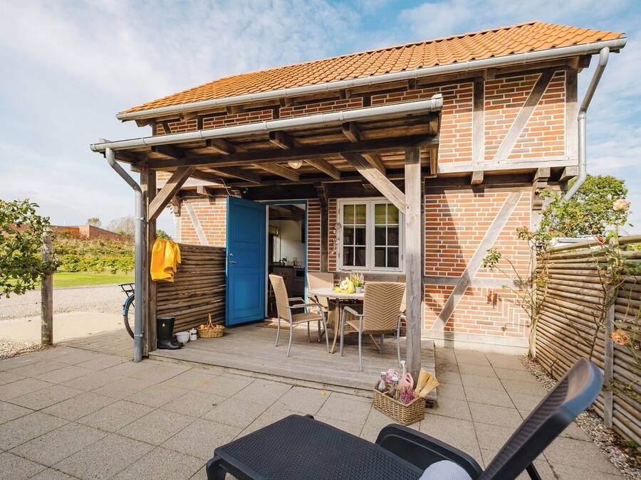 A brick house with a tiled roof, a covered patio with outdoor furniture, and a garden area.
