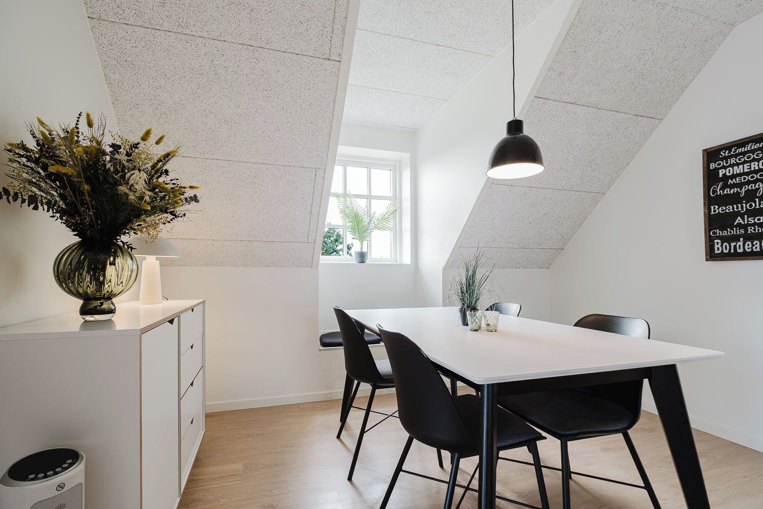 A modern dining area with a white table, black chairs, a pendant light, and a decorative plant.